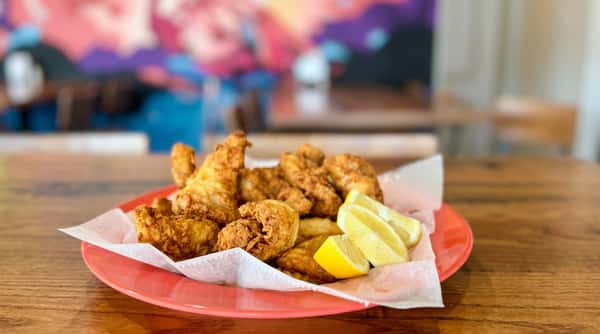 Fried fish and chips with several lemon wedges on a coral-colored plate lined with paper.