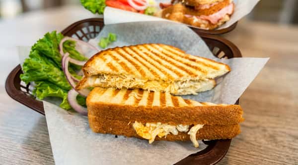 Grilled chicken panini, cut in half, with visible cheese and chicken, served on parchment paper with lettuce and red onion in the background.
