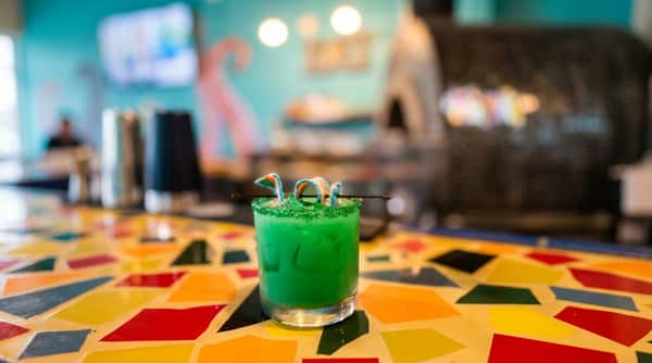 Green cocktail with a sugared rim and candy garnish, on a mosaic tile table.
