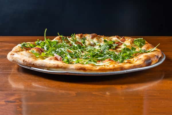 Thin-crust pizza topped with melted cheese, fresh greens and herbs, served on a wooden table.