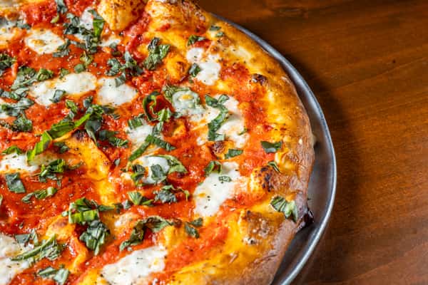 Close-up of a freshly baked pizza topped with melted cheese, tomato sauce, fresh herbs and assorted toppings.