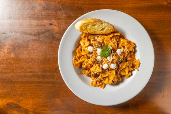 Plate of pasta topped with a rich sauce, grated cheese and fresh herbs, served on a wooden table.