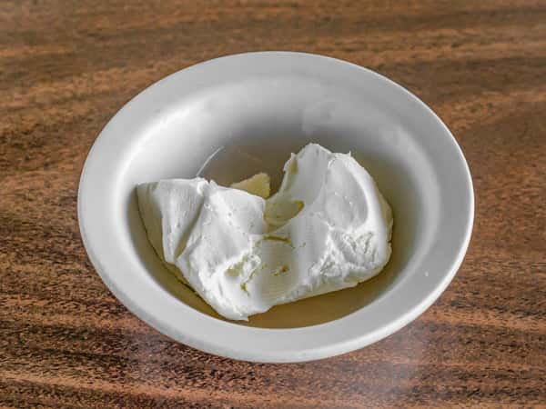 Side of fresh white cream cheese from Miller's Cafe served in a white bowl on a dark wood table.