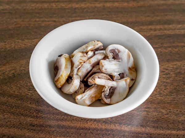 White bowl of sliced sauteed mushrooms side dish served on a dark wood table at Miller's Cafe.