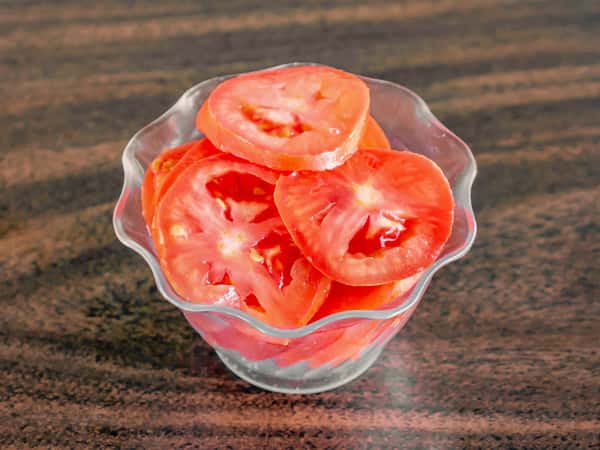 Bright red sliced tomatoes served in a wavy glass bowl on a dark wood table at Miller's Cafe.