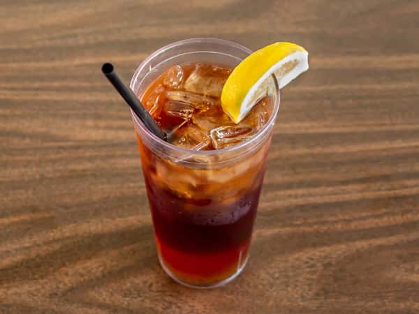 Iced tea or brown mixed drink in a plastic cup with a lemon slice and straw on a wooden table at Miller's Cafe.