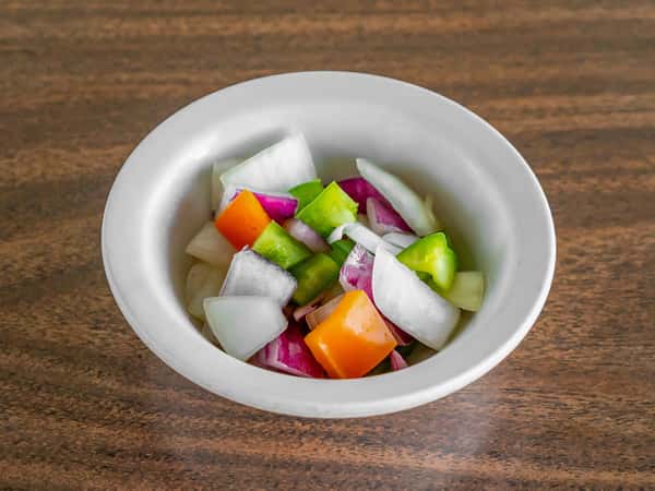 Colorful chopped white and red onion, green, and orange pepper garnish in a white bowl at Miller's Cafe.