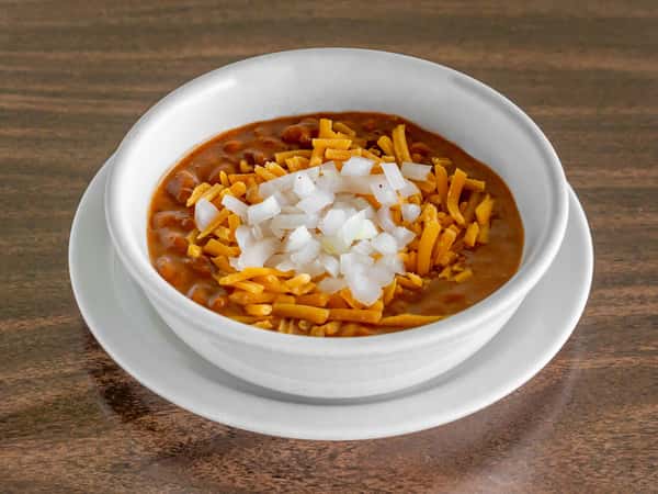 Miller's Cafe hearty chili bowl topped with shredded cheddar cheese and diced white onions on a dark wood table.