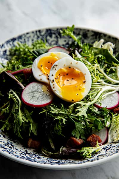 Salad topped with a soft boiled egg, sliced radish, and bacon bits