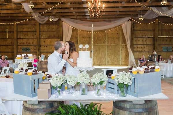bride and groom kissing in front of the wedding cake in a barn