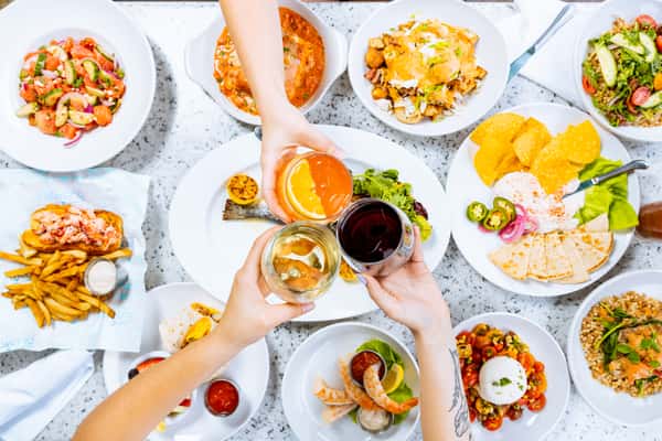 Hands cheering drinks over a table full of food