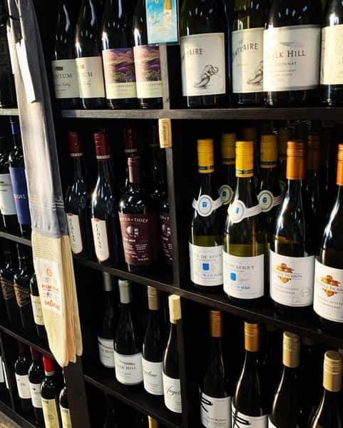 Wine shelf display featuring a variety of red and white wines, with a towel that reads “Cookin’ the calories not countin’ them.”