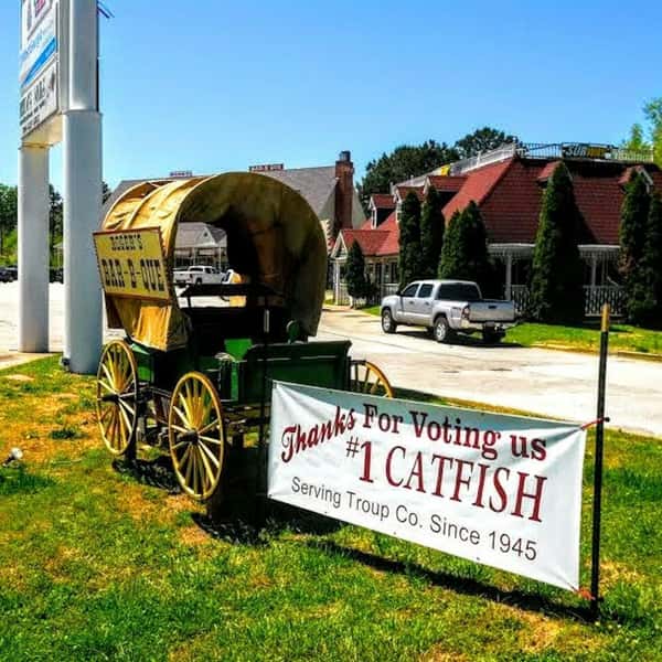 Covered wagon with "Bar-B-Que" signage beside a banner thanking customers for voting them #1 catfish in Troup County.