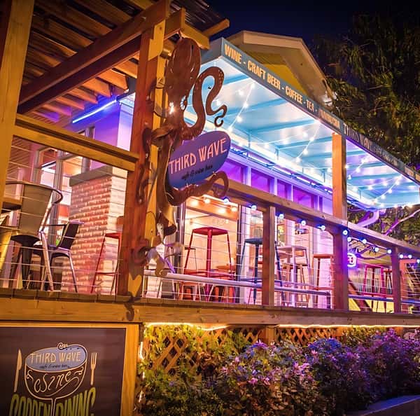 Exterior view of Third Wave Café & Wine Bar featuring octopus signage, balcony seating, and vibrant evening lighting.