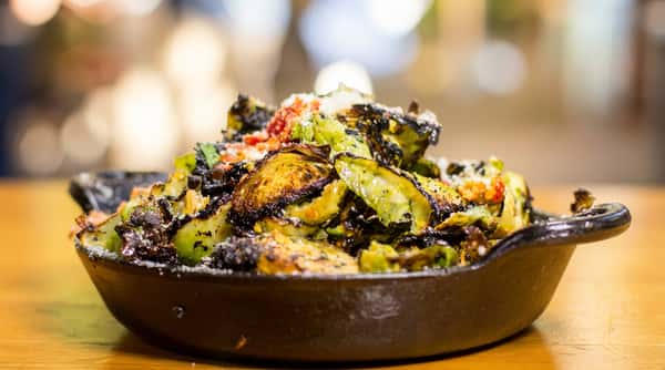 Crispy roasted Brussels sprouts finished with parmesan and house seasoning, served in a cast-iron skillet for a bold and savory small plate.