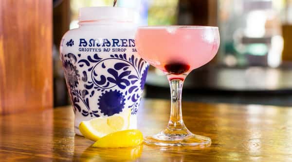 A chilled pink cocktail served in a coupe glass with cherry garnish, offering a bright and refreshing flavor profile.