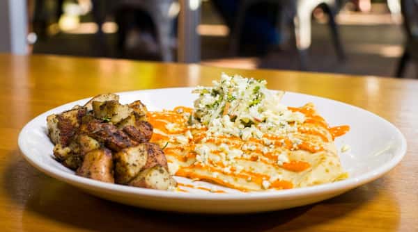 A savory brunch plate featuring eggs with house-made sauce, roasted potatoes, and fresh slaw.