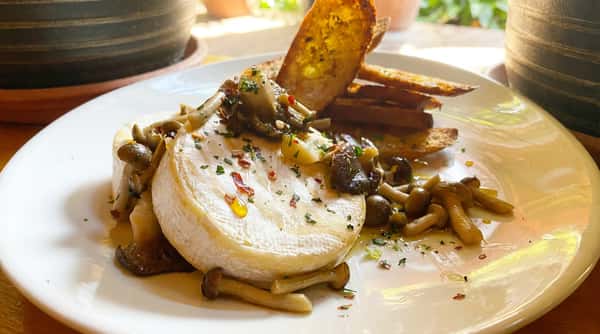 Warm baked brie topped with sautéed mushrooms, herbs, and a drizzle of olive oil, served with toasted crostini for a rich and savory appetizer.