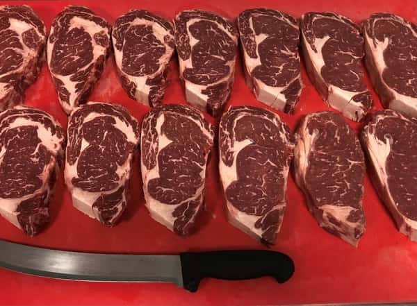 assortment of raw meat on a cutting board with a knife