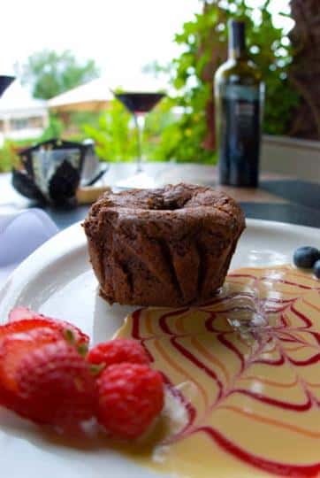 Chocolate lava cakes served with strawberries on a patio table with a lgass of wine in the background