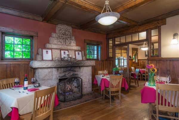 Interior shot of the dining hall with a big stone fireplace and tables set all around
