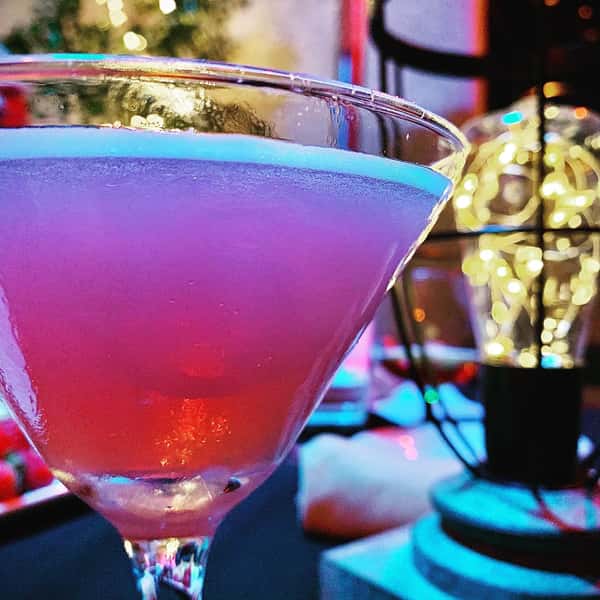 Close up of pink colored cosmopolitan cocktail in martini glass next to table lantern