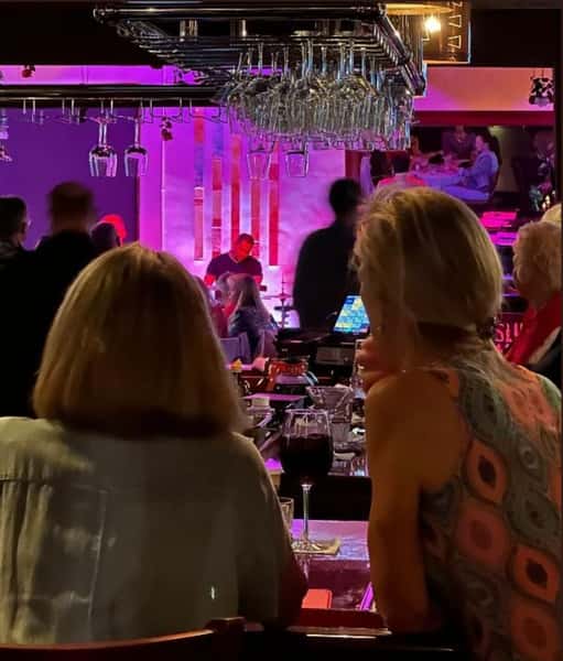 Crowed Bar scene with fore front back of two seated women in distance dfrummer in band playing in the lounge room