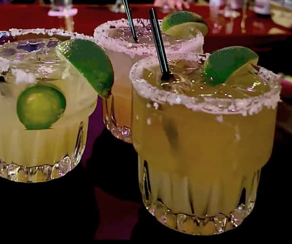 photo of 3 vickyrita cocktails in hiball glasses with wedge of lime on bar top