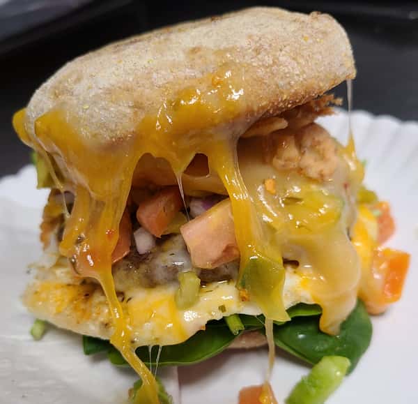 Dripping melted orange cheese covers a breakfast sandwich with an egg, patty, and colorful vegetables.