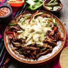 Plate of sizzling beef fajitas with melted cheese and sautéed peppers.
