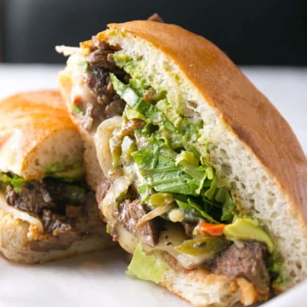 Mexican torta sandwich filled with grilled beef, guacamole, lettuce, and melted cheese on a toasted bun.