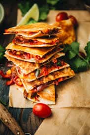 Pile of cheesy quesadillas filled with vegetables and served on parchment paper with cherry tomatoes and cilantro.