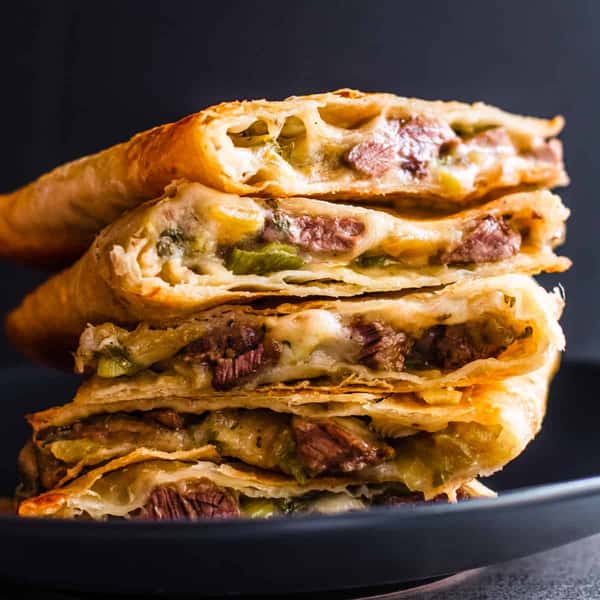 Quesadillas filled with grilled steak, peppers, and melted cheese, stacked on a dark plate.