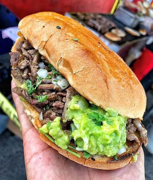 Mexican torta filled with beef, chopped onions, cilantro, and guacamole