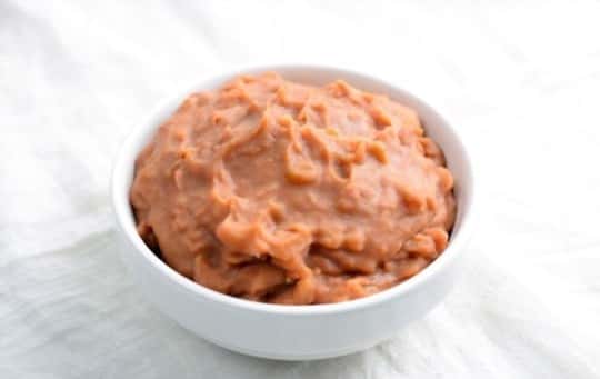 Bowl of creamy refried beans on a white cloth background.