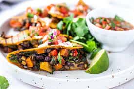 Crispy tacos filled with vegetables, beans, and sweet potatoes, served with salsa on the side.