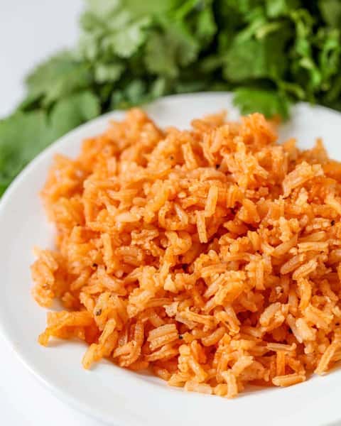 Plate of Mexican rice with a vibrant orange hue, served with fresh cilantro in the background.