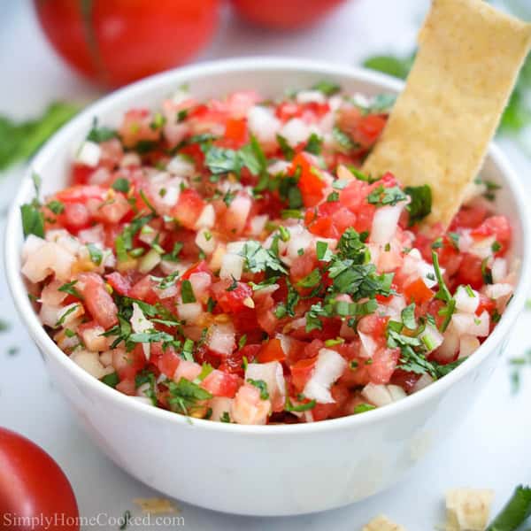 Bowl of fresh pico de gallo with diced tomatoes, onions, and cilantro, served with a tortilla chip.