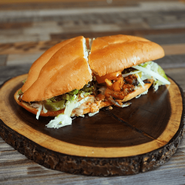 Mexican torta sandwich filled with grilled meat, lettuce, and pickled jalapeños on a rustic wooden plate.