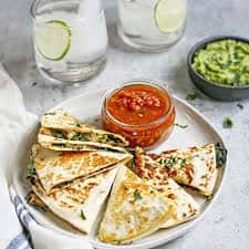 Quesadillas served with salsa in a jar, surrounded by guacamole and drinks with lime.