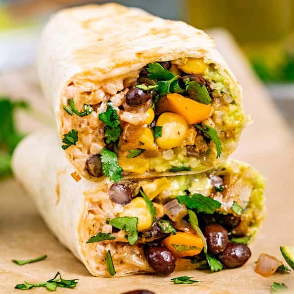 Vegetarian burrito cut in half, filled with black beans, corn, rice, guacamole, and vegetables.