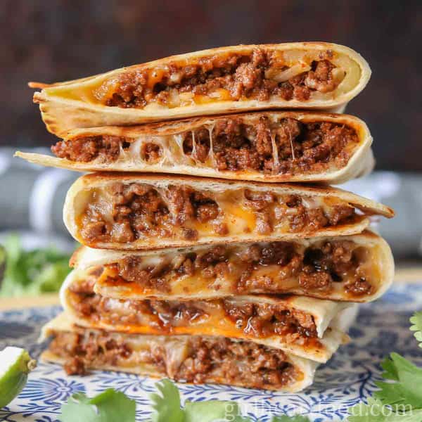 Stack of quesadillas filled with seasoned ground beef and melted cheese, cut in halves and layered on a plate.
