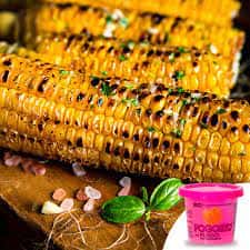 Grilled corn on the cob garnished with herbs and coarse salt, with a tub of seasoning on the side.