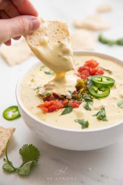 Queso dip with melted cheese, tomatoes, jalapeños, and tortilla chip being dipped