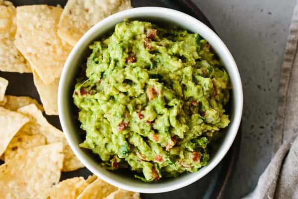 Fresh guacamole with chopped tomato and cilantro in a bowl, surrounded by tortilla chips.