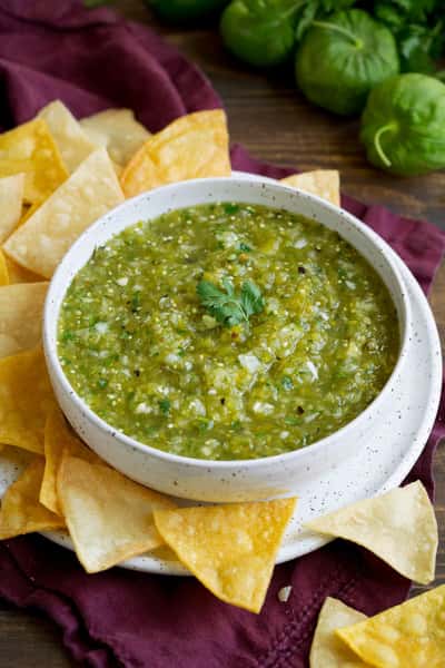 Bowl of green salsa verde surrounded by yellow corn tortilla chips.