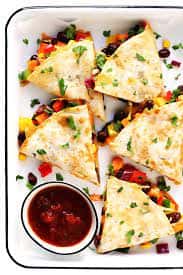Vegetarian quesadillas cut into triangles, served with salsa in a white tray.