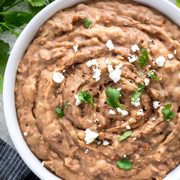 Bowl of creamy refried beans topped with crumbled cheese, black pepper, and fresh cilantro.