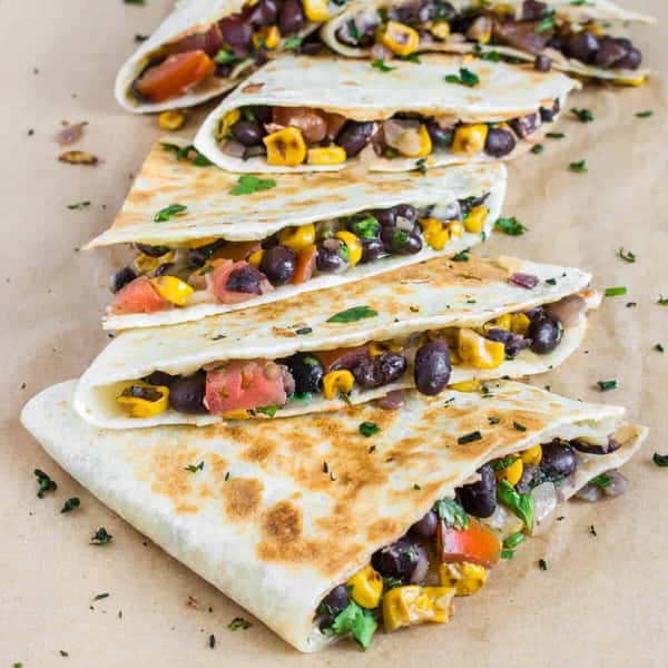 Grilled quesadillas stuffed with black beans, corn, tomatoes, and herbs, arranged on parchment paper.