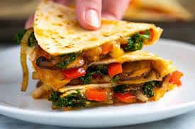 Stacked quesadilla slices filled with sautéed vegetables, cheese, and vibrant colors on a white plate.